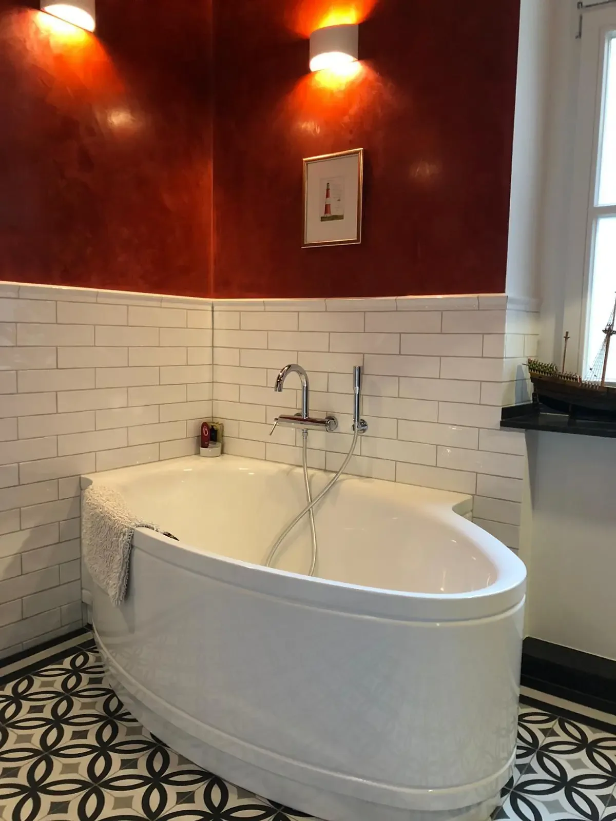Freistehende Badewanne vor einer roten Wand mit weißen Metrofliesen