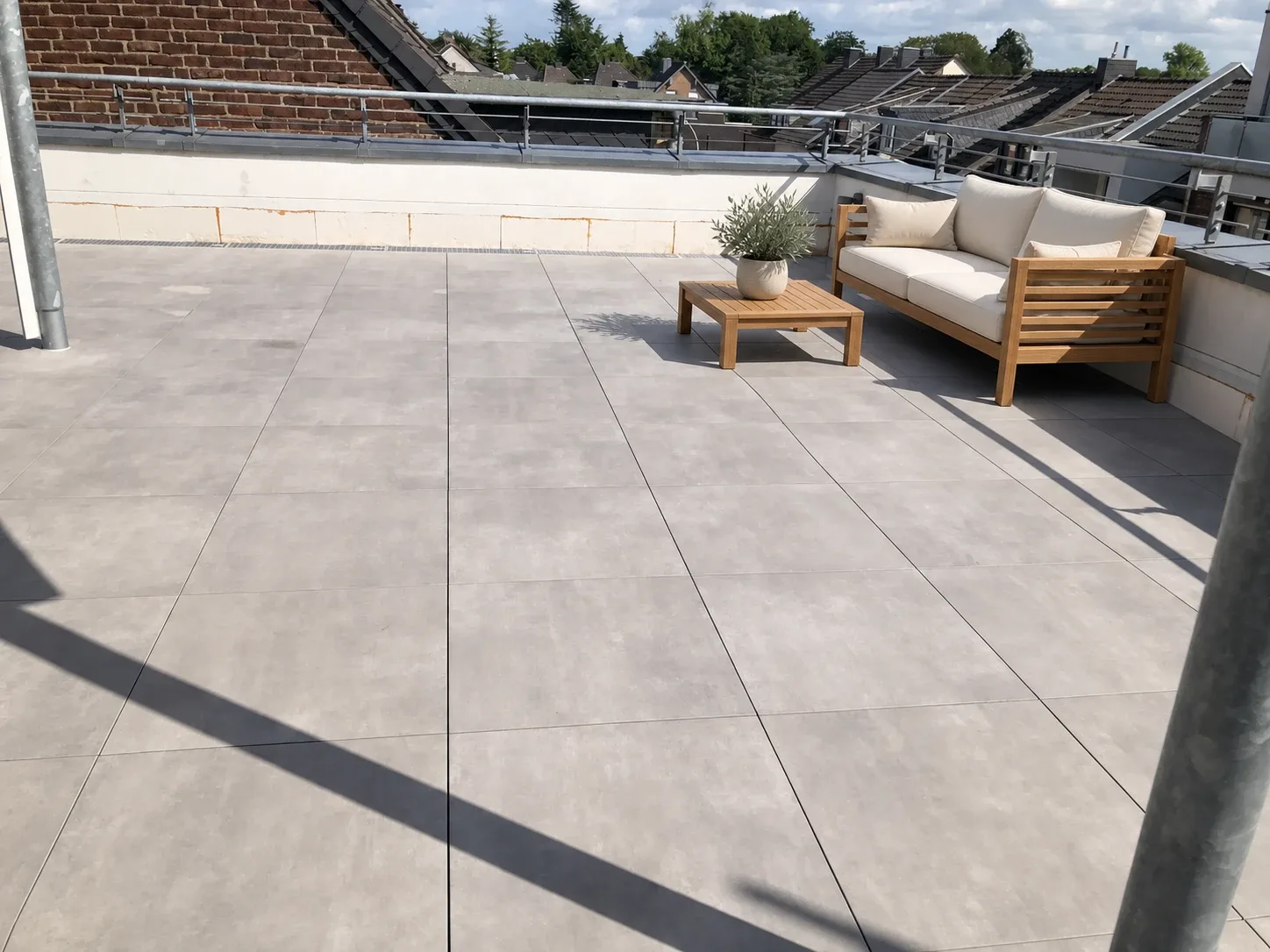 Dachterrasse mit grauem Plattenbelag; Sitzmöbel und Pflanze mit KI ergänzt