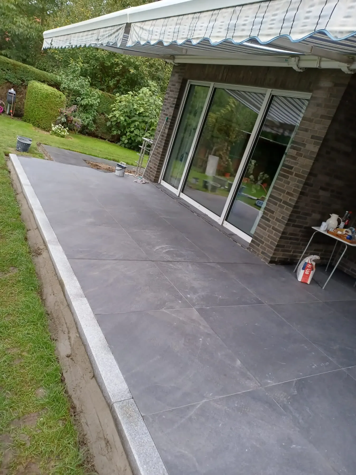 Anthrazitfarbener Terrassenbelag vor einem Wintergarten
