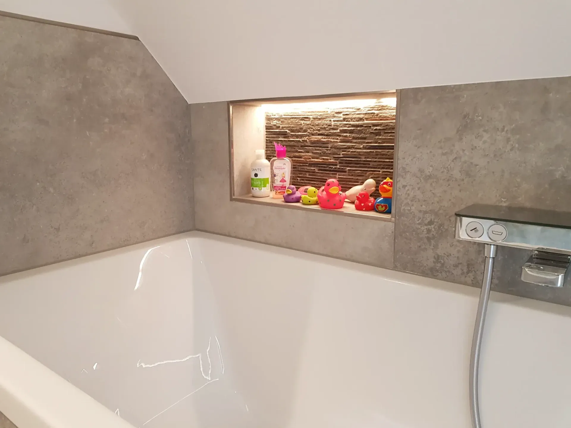 Badewanne mit beleuchteter Ablagenische und grauen Wandfliesen