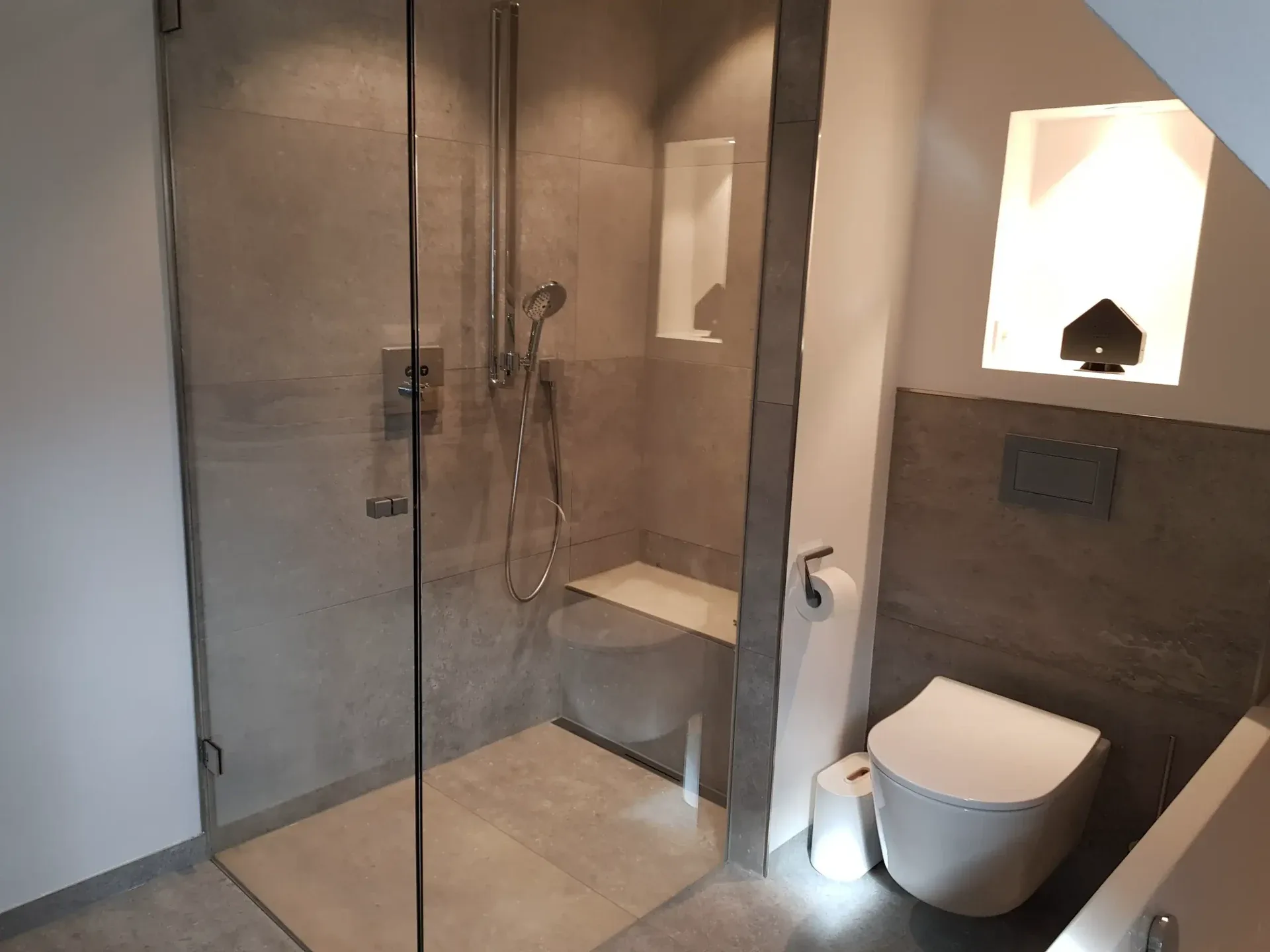 Dusche mit Glaskabine, Sitzbank und grauem Fliesenbelag
