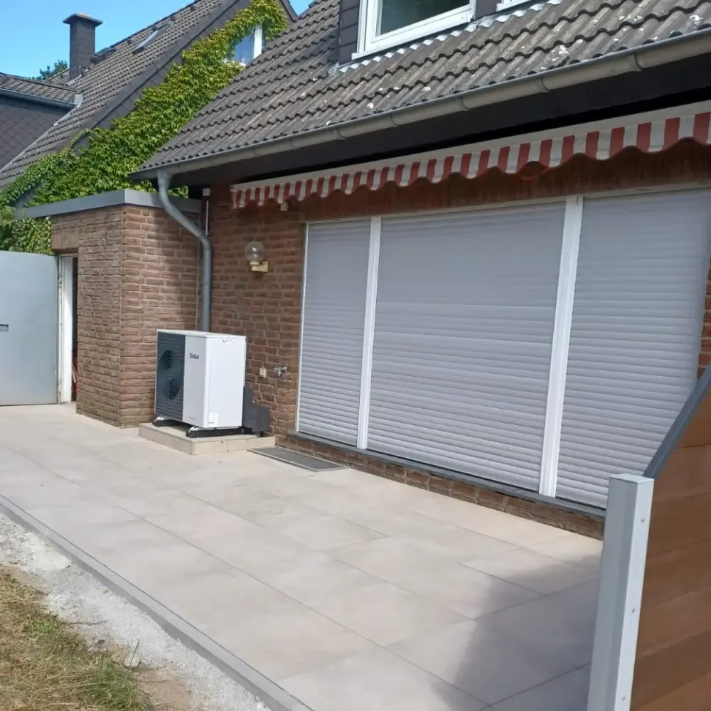 Helle Terrassenplatten vor einem Wohnhaus mit Markise