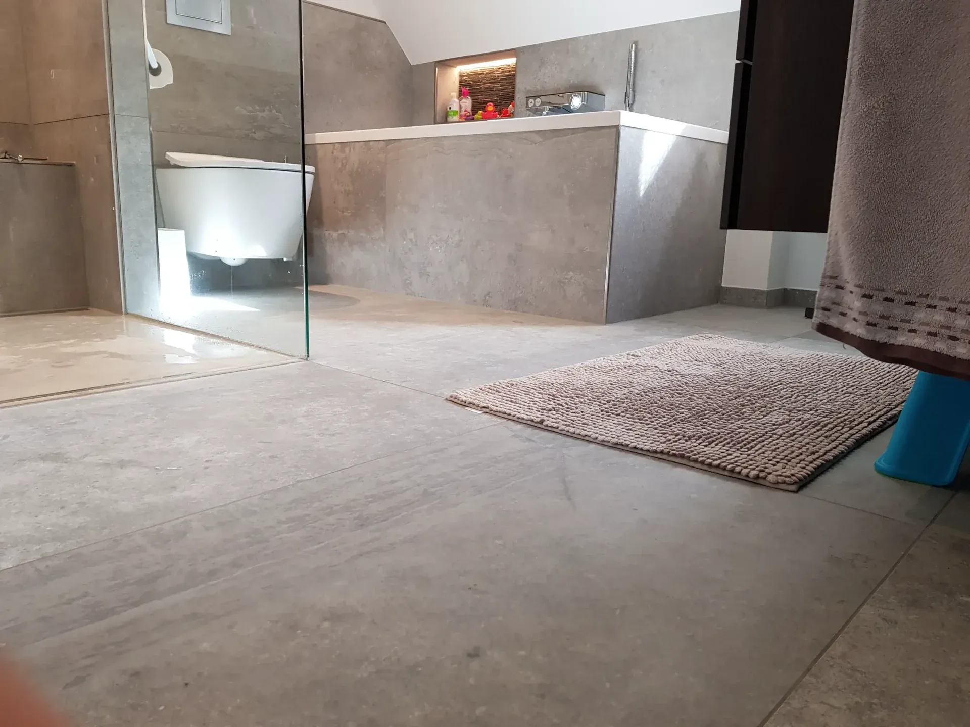 Grauer Duschbereich mit Glasabtrennung neben einer Badewanne