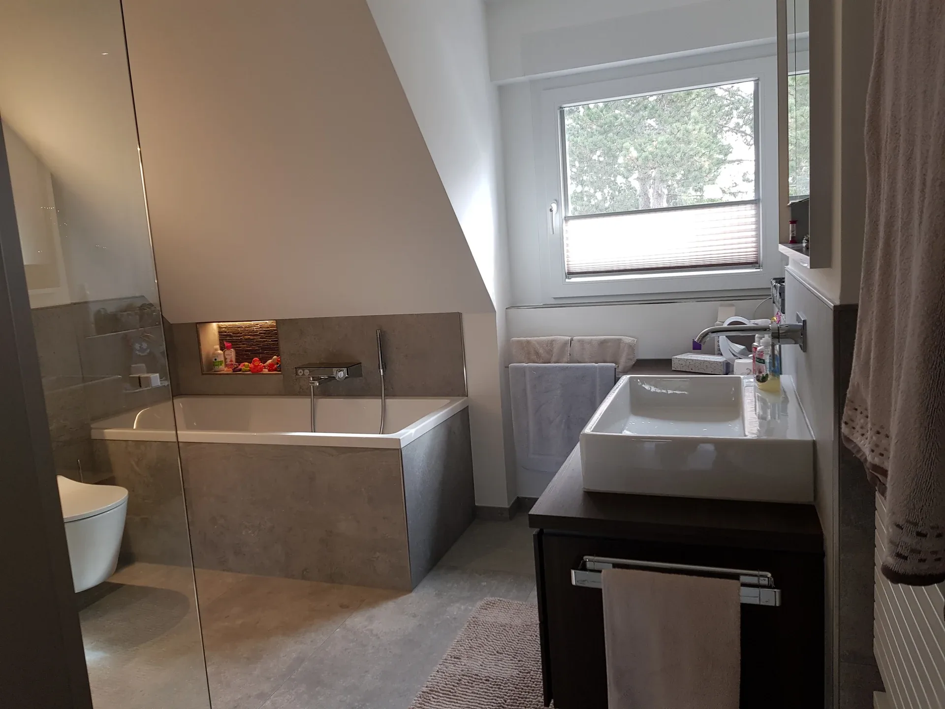 Fertiges graues Badezimmer mit Badewanne und Glasdusche